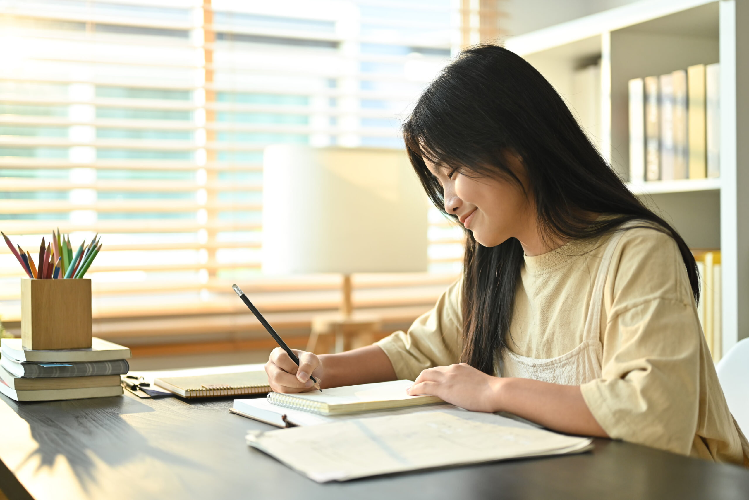 Middle-school student writing narration in a notebook at a sunlit desk with books and pencils.