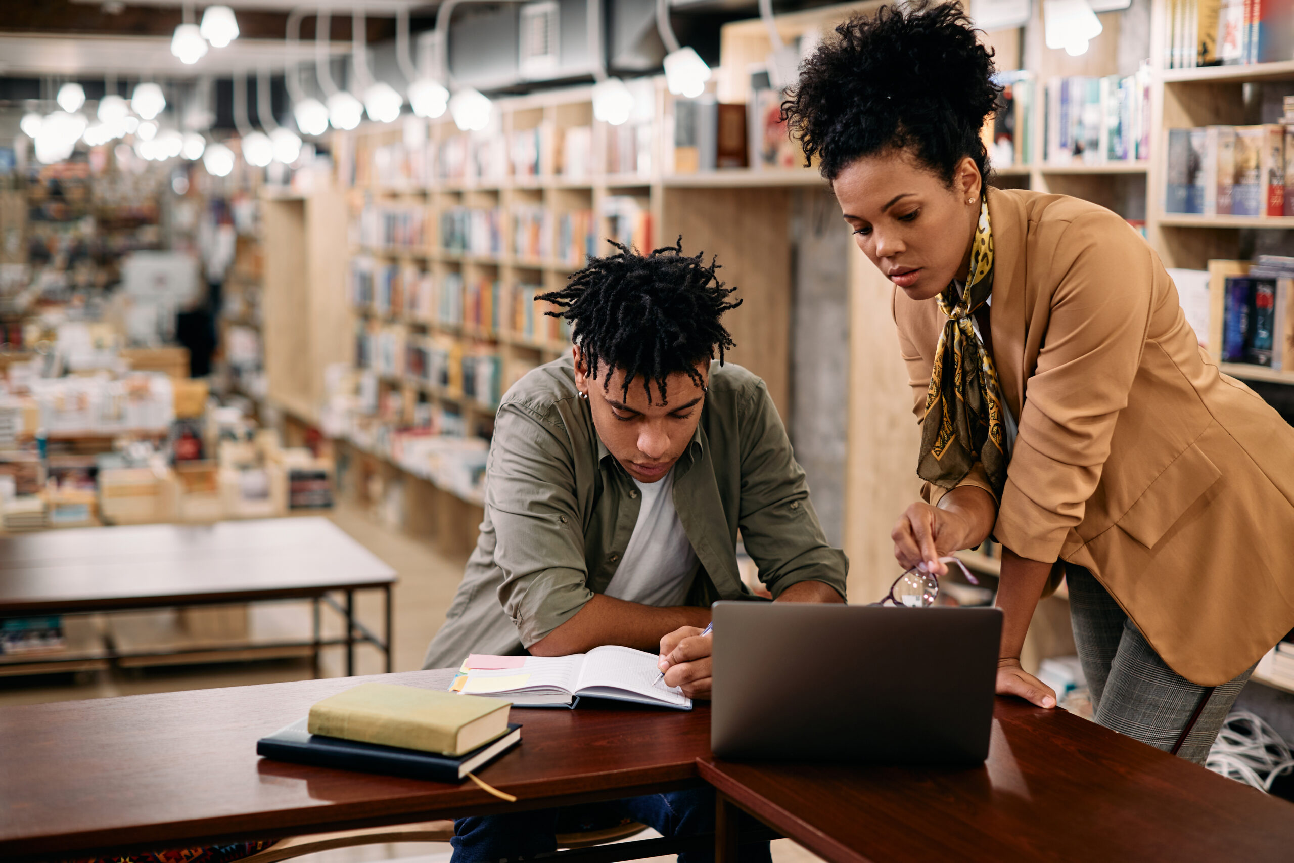 A teacher mentors a student through thoughtful study in a quiet library, representing the Ars Cogitans™ approach to vocation and creative confidence.