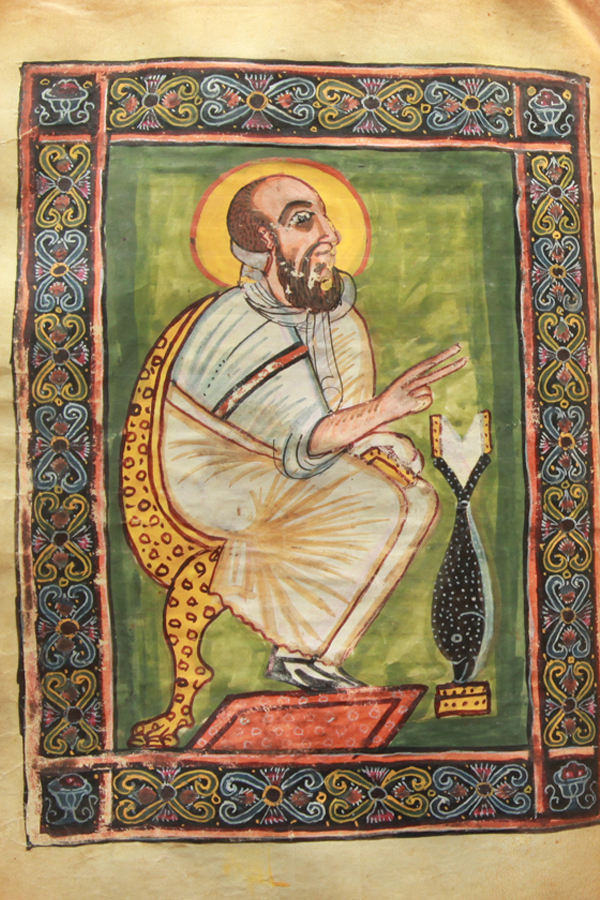 Ethiopian illuminated manuscript page from the Abba Garima Gospels showing a haloed evangelist seated with blessing gesture, ornate border.