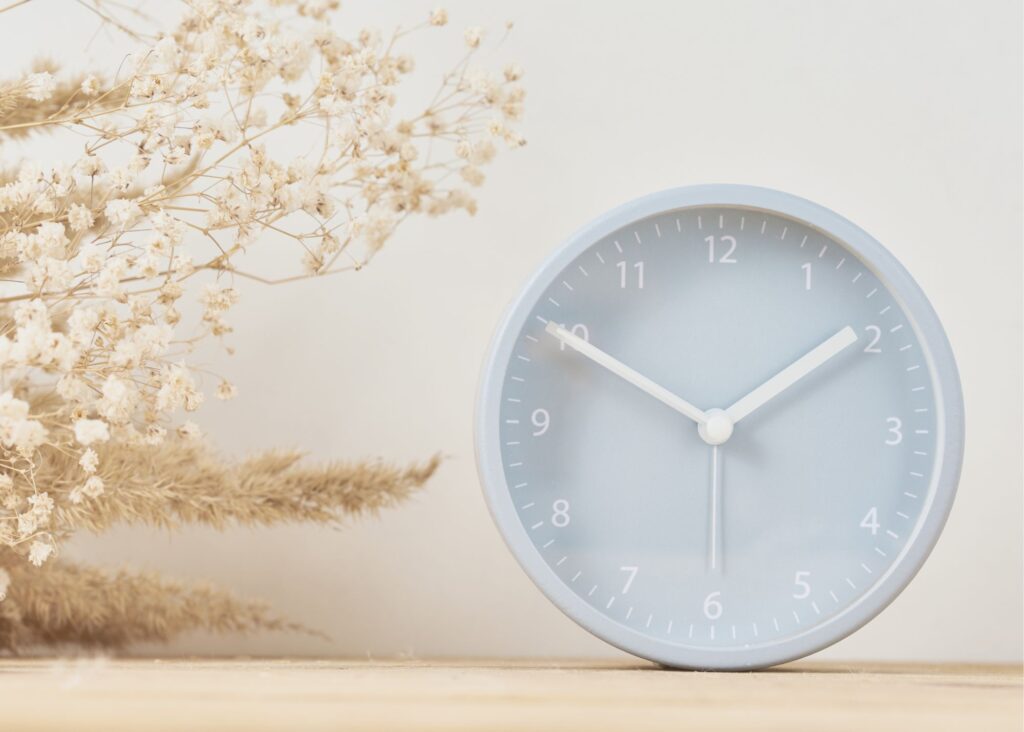 Minimal round desk clock on wood with dried flowers against a soft neutral background.