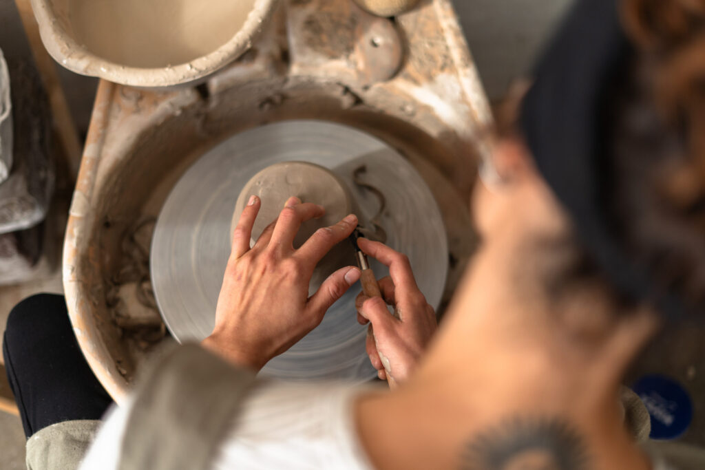 Close-up of hands trimming a clay bowl on a pottery wheel—quiet, focused work.