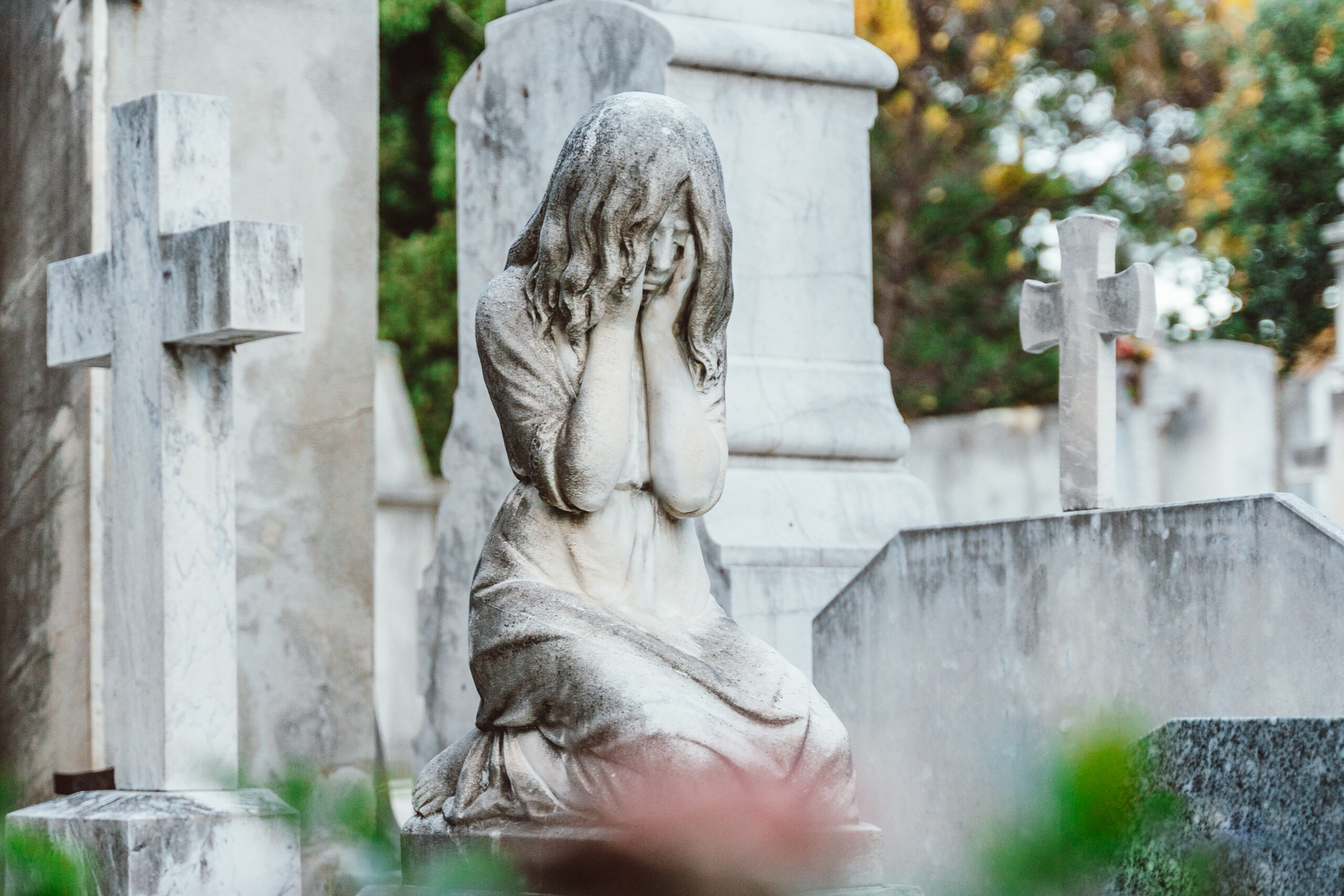 Marble statue of a woman weeping in a cemetery, flanked by stone crosses, evoking October grief and quiet lament.