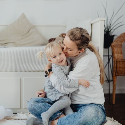 A mother sitting on the floor hugging her young daughter during a peaceful homeschool morning.