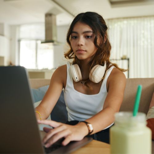 A teenage girl works quietly on a laptop at home, representing the emotional journey of homeschooling an oppositional teen daughter.
