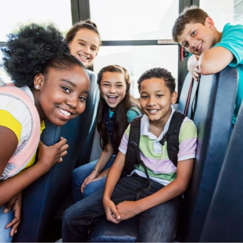 A group of smiling children on a school bus, representing a child who thrives in public school while siblings learn at home.