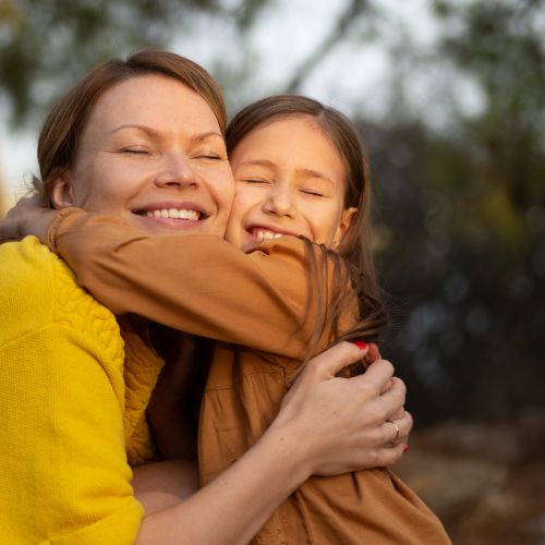 A mother and daughter hugging outdoors at sunset, eyes closed and smiling, expressing warmth and peace during a gentle homeschool day.
